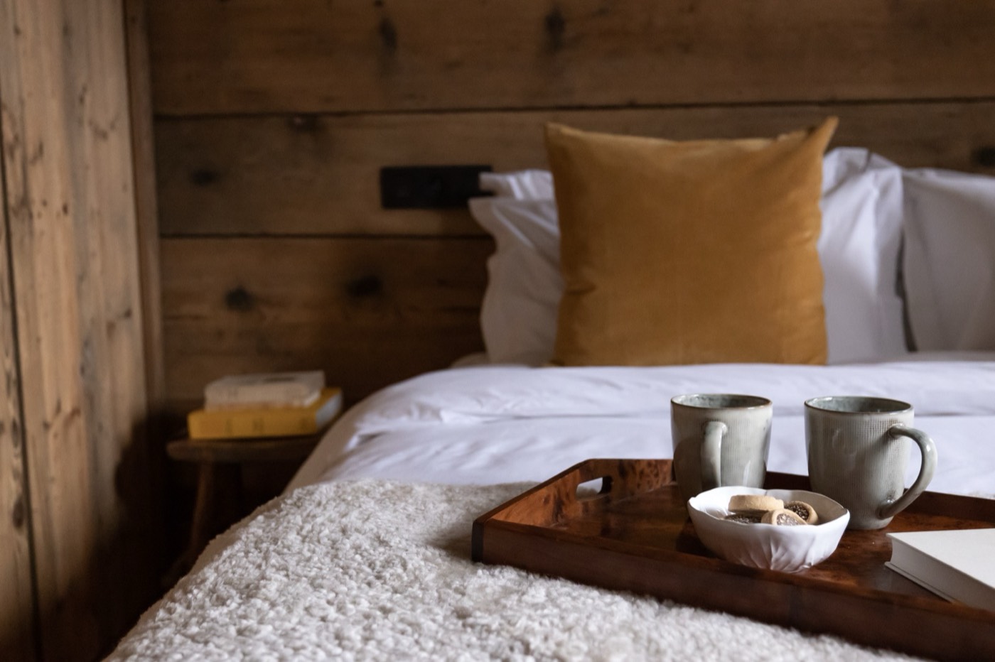 Een slaapkamer met houten wanden, een bed met wit linnen en een dienblad met koffie