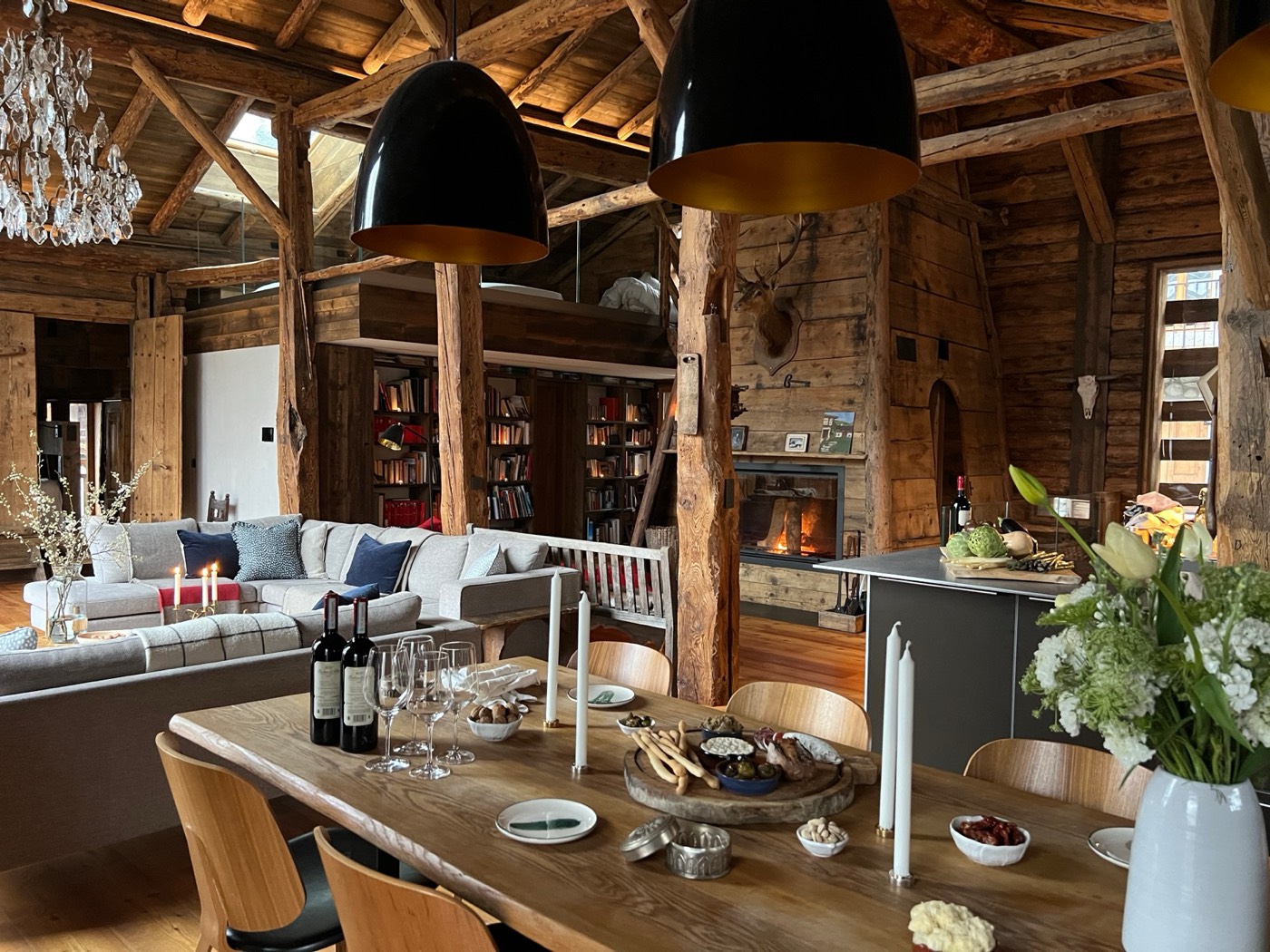 De open woonruimte met een lange houten tafel, de haard en boekenkasten onder oude balken