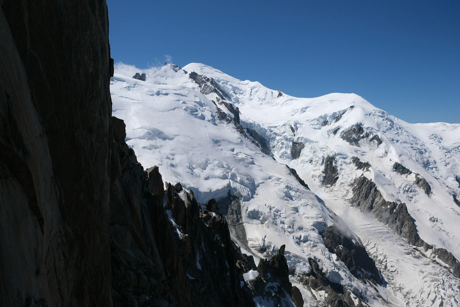 De besneeuwde Mont Blanc achter donkere rotswanden, blauwe lucht