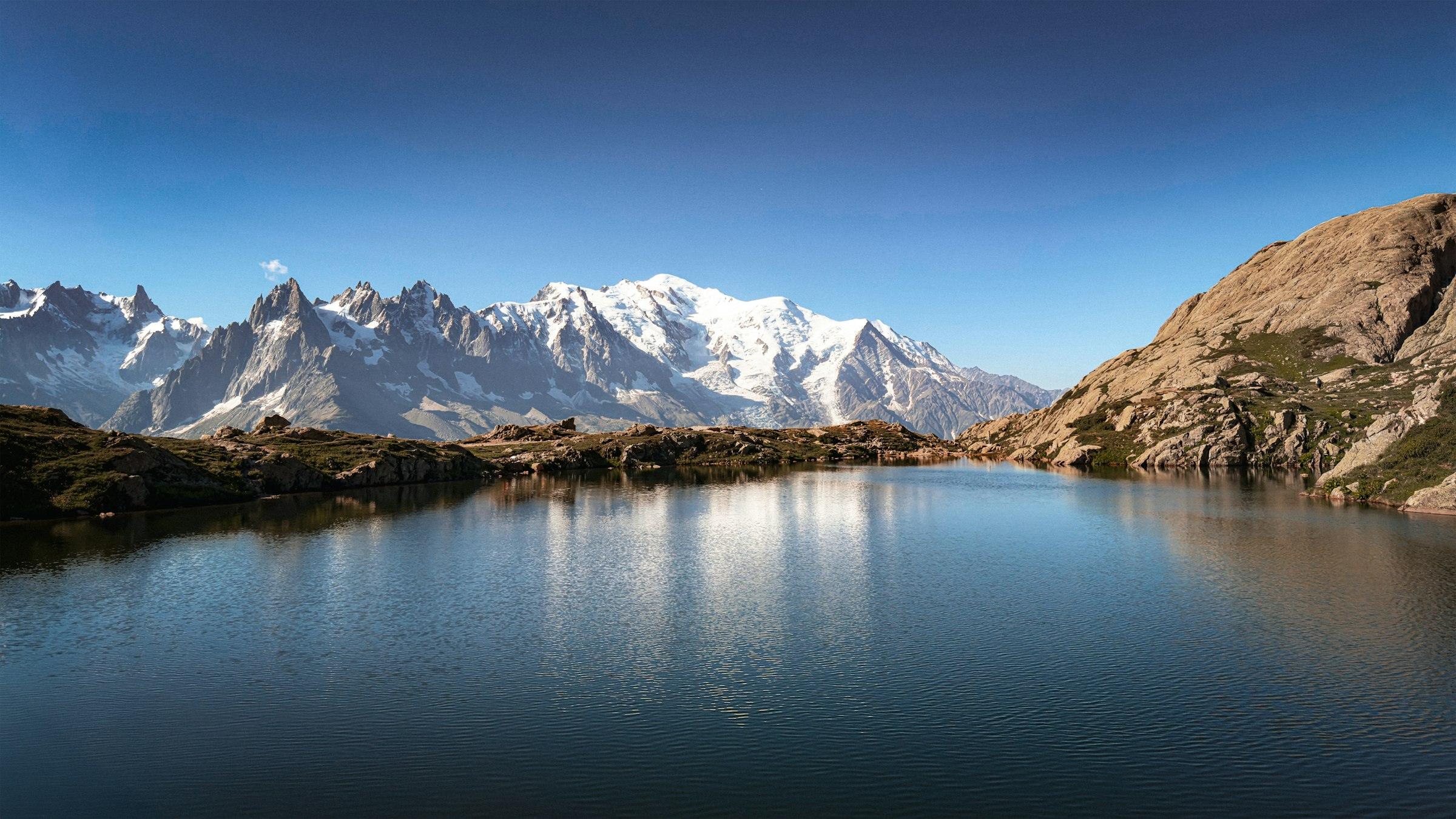 Een bergmeer met de Mont Blanc en rotspieken in de verte, strakblauwe lucht